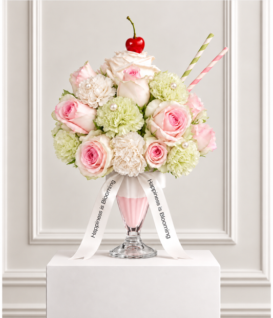 Le Pistache Rose flower frappé: blush pink roses with pale green and ivory carnations and faux pearls in a sundae glass, topped with a white rose whipped cream and a cherry, with pink and green striped straws and Happiness is Blooming ribbons